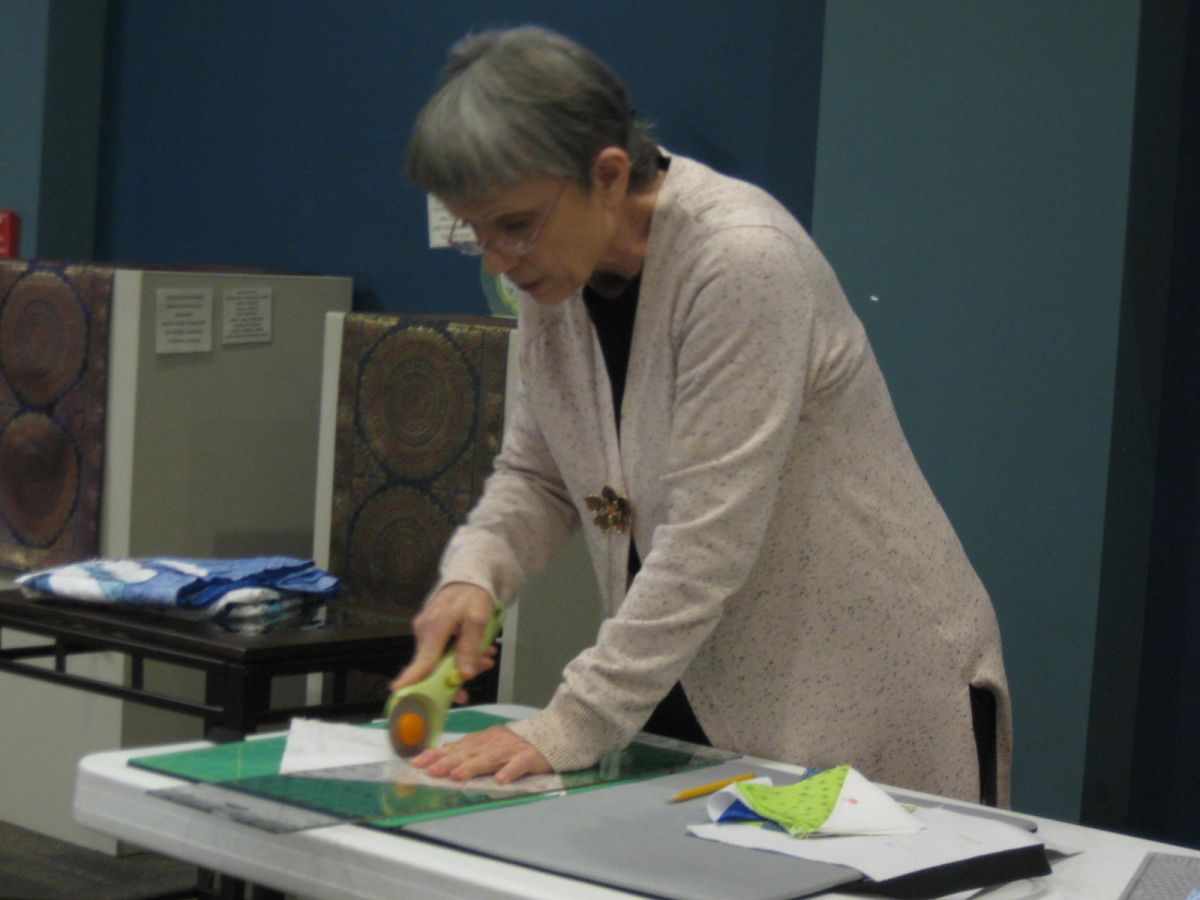 Demonstrator Judith Diver cuts fabric with her rotary tool turning 2 10-inch squares into 8 4-inch half-triangle squares